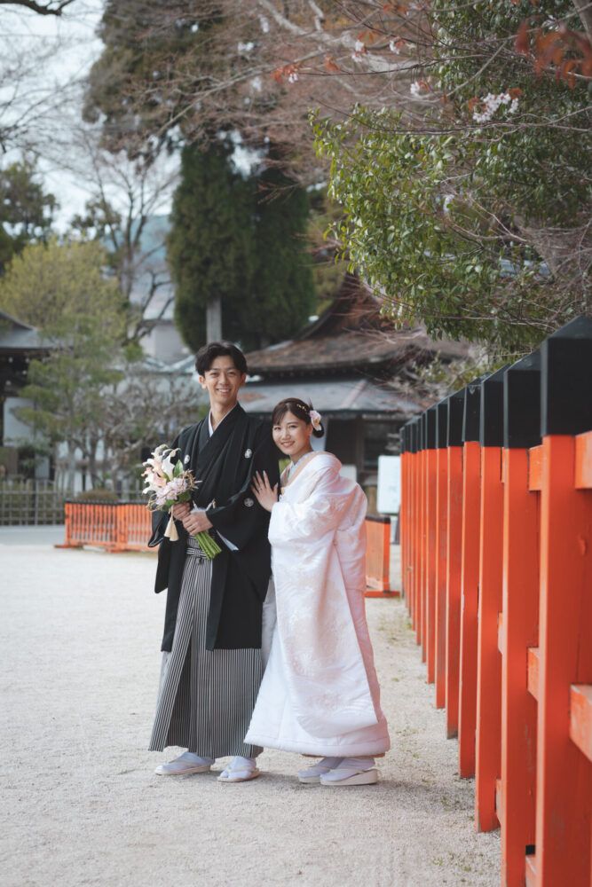 上賀茂神社の朱塗りの塀を横手に白無垢の花嫁と新郎