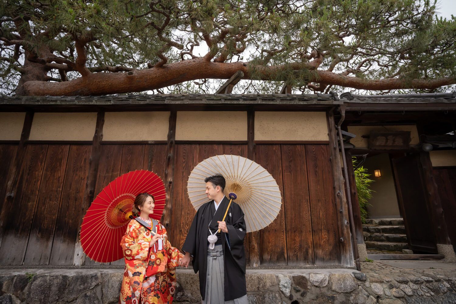 八坂の塔周辺の木塀前で紅白の番傘を持って色打掛の花嫁と新郎