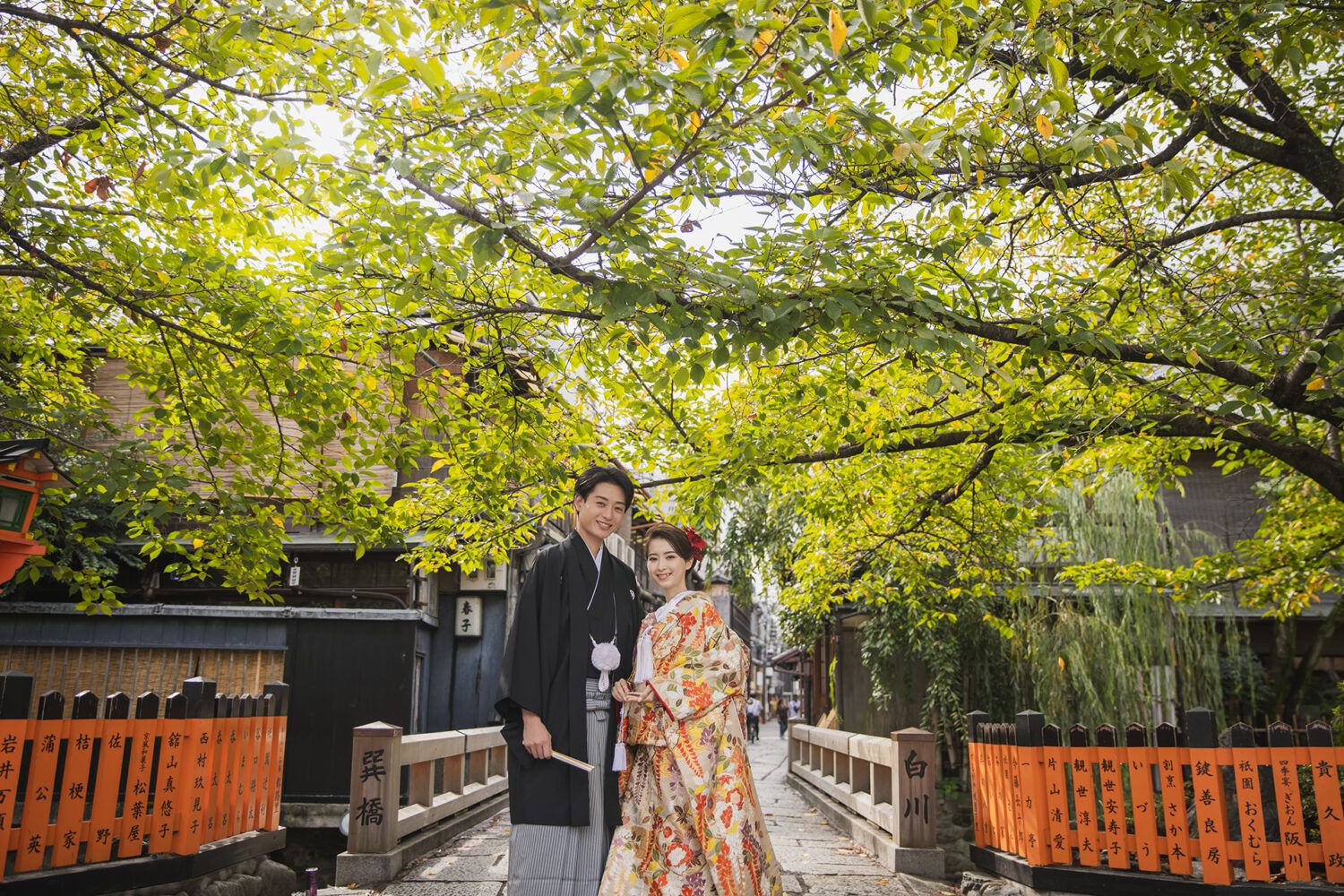祇園の巽橋と緑を背景での色打掛の花嫁と新郎