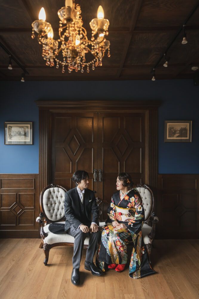 英国アンティークスタジオでウイリアムノリスの壁紙を背景にカンタベッラドレス(Cannta Bella Dress）の花嫁と新郎