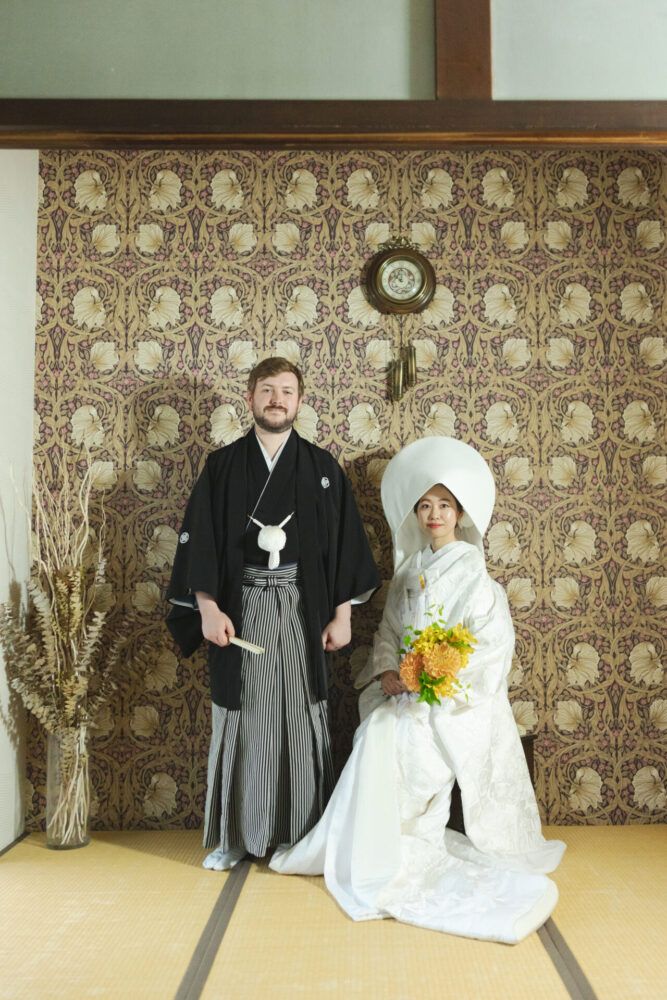 京町家のエントランスでウイリアムノリスの壁紙を背景に綿帽子姿の白無垢の新郎新婦