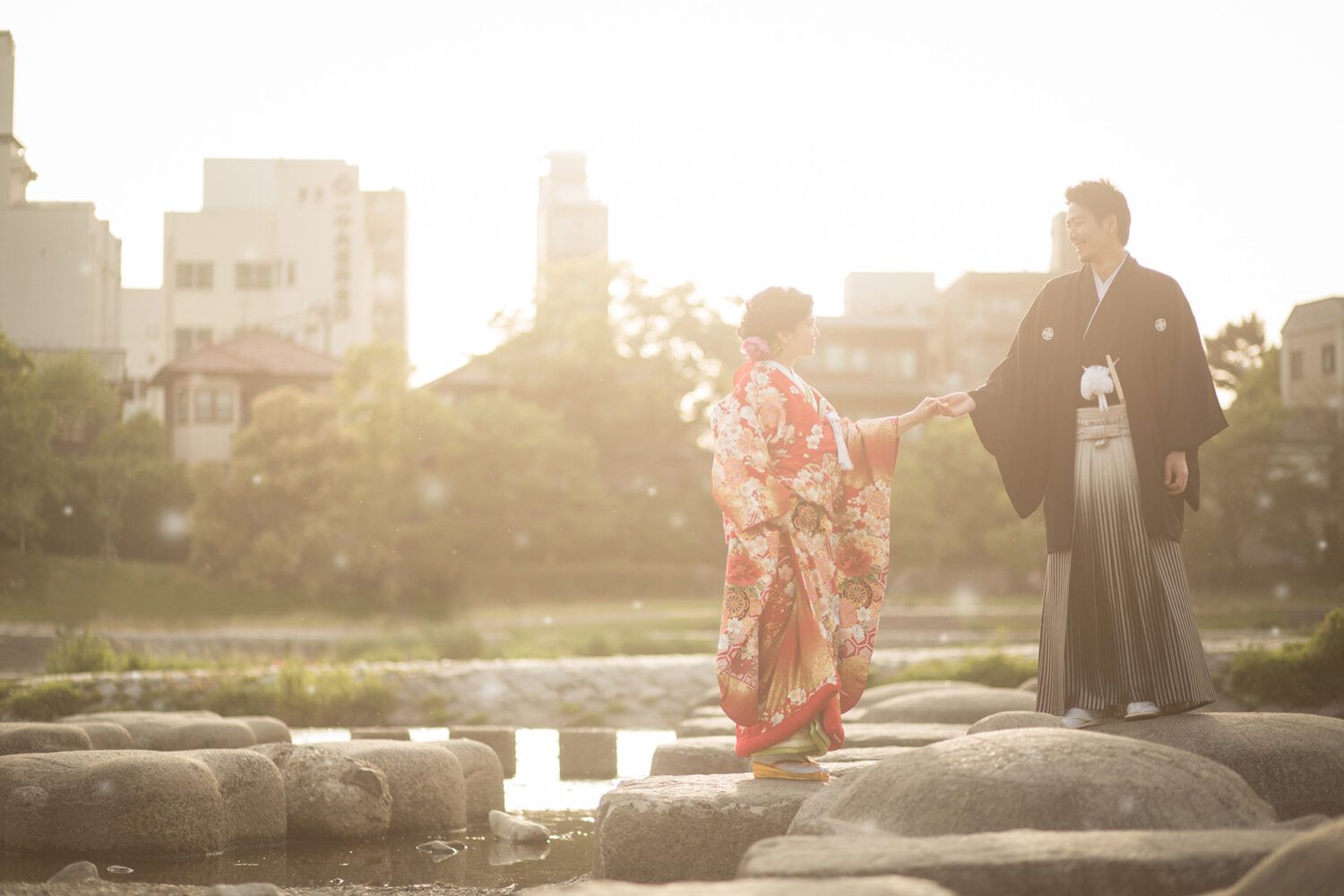 夕日の中、鴨川の石の上で手を取り合う新郎新婦