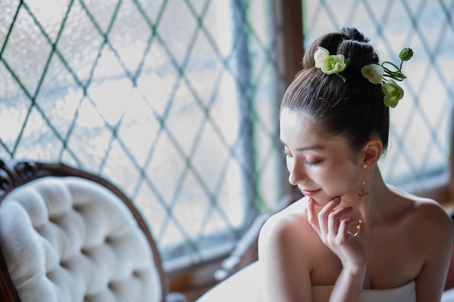 英国アンティークスタジオのステンドガラスを背景にソファに座ったカンタベッラドレス(Cannta Bella Dress）の花嫁