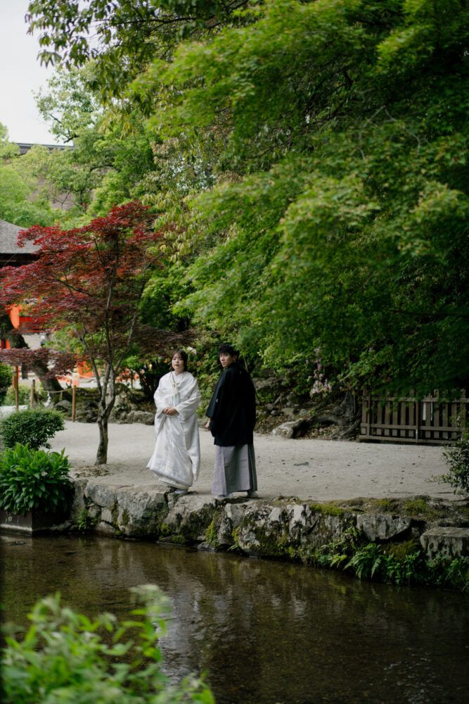 上賀茂神社の川のせせらぎを見つめる白無垢の花嫁と新郎