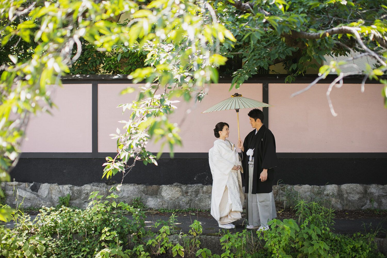 平安神宮周辺の白川疎水のたもとで白番傘を持って見つめあう新郎新婦