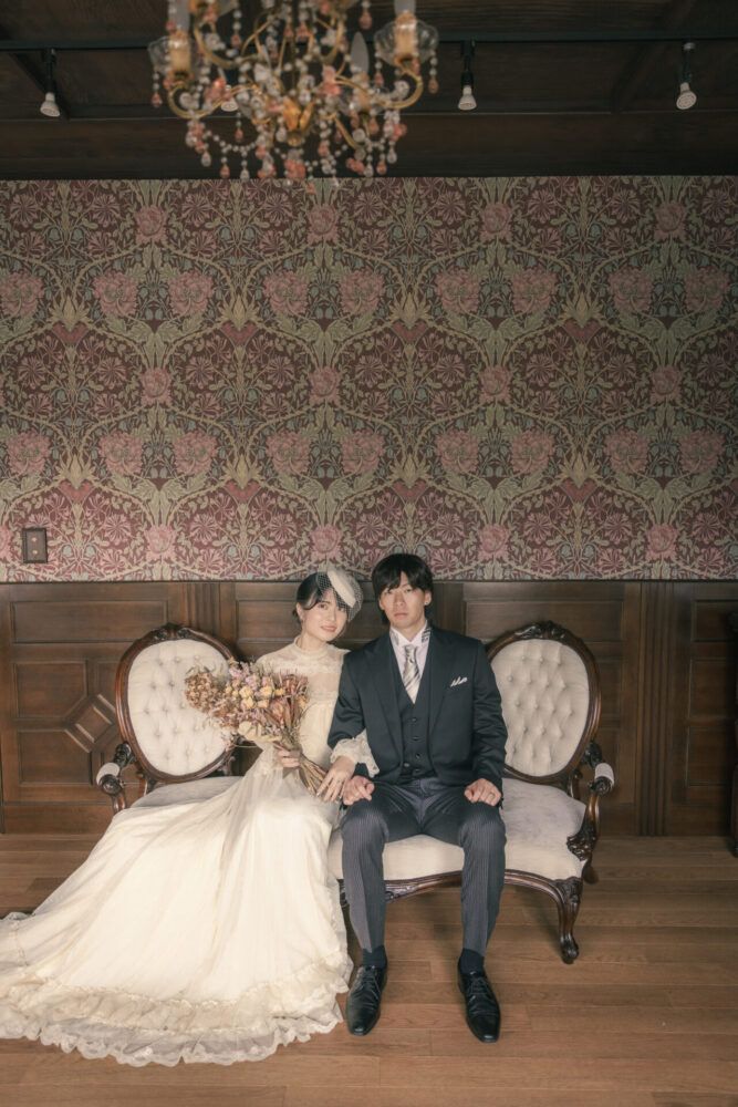 英国アンティークスタジオのウイリアムノリスの壁紙を背景にヴィンテージドレスでの花嫁と新郎