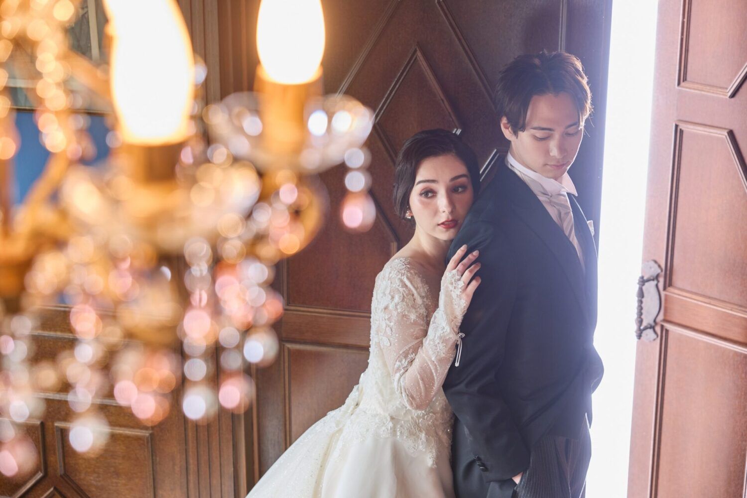 英国アンティークスタジオの扉から光が差し込むカンタベッラドレス(Cannta Bella Dress）の花嫁と新郎