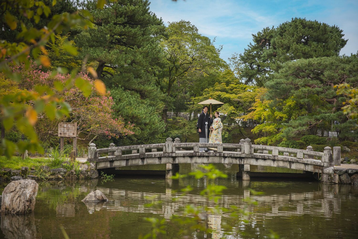 円山公園のひょうたん池の橋の上を白番傘を持った新郎新婦