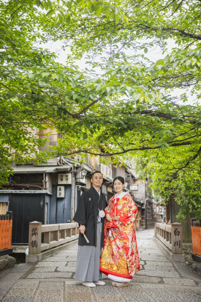 祇園の巽橋と緑を背景で色打掛の花嫁と新郎