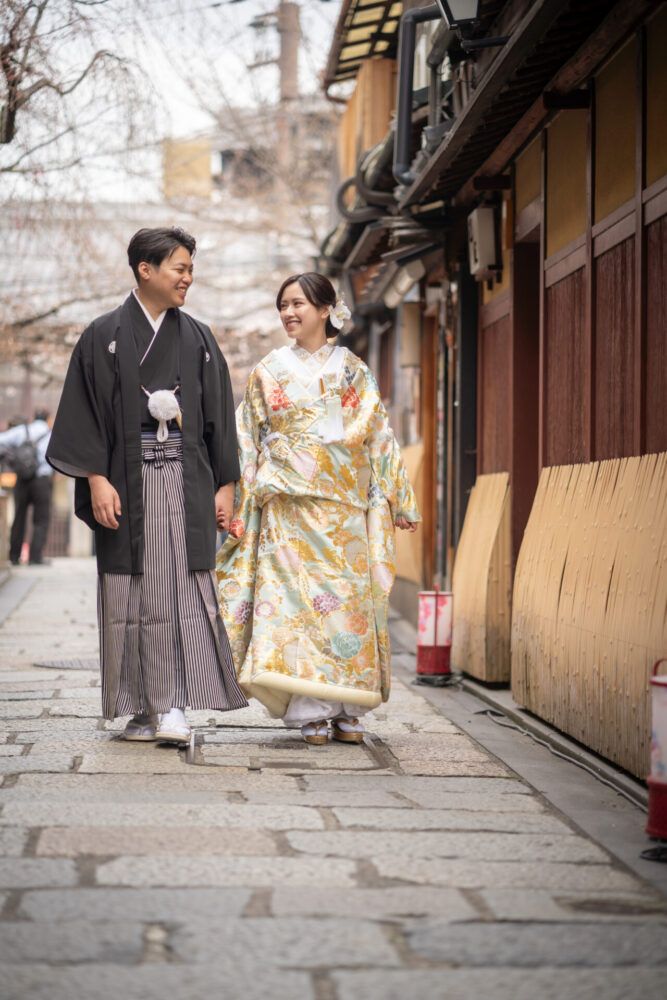 祇園街の石畳を歩く色打掛の花嫁と新郎