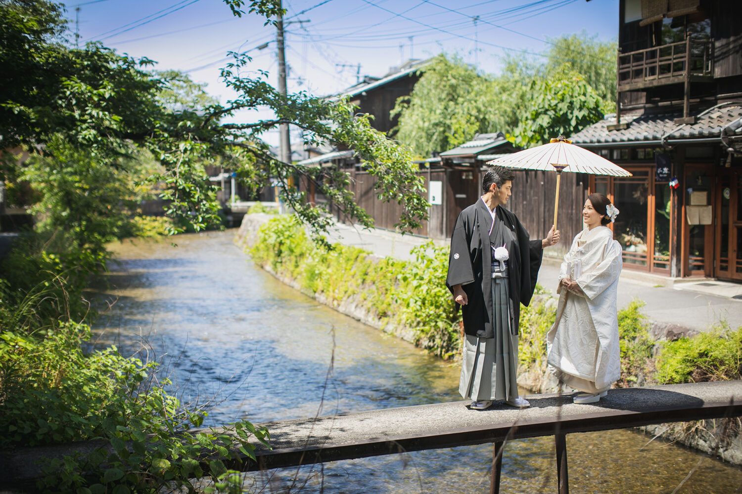 平安神宮周辺の白川疎水のもっこ橋で白番傘を持った白無垢の花嫁と新郎