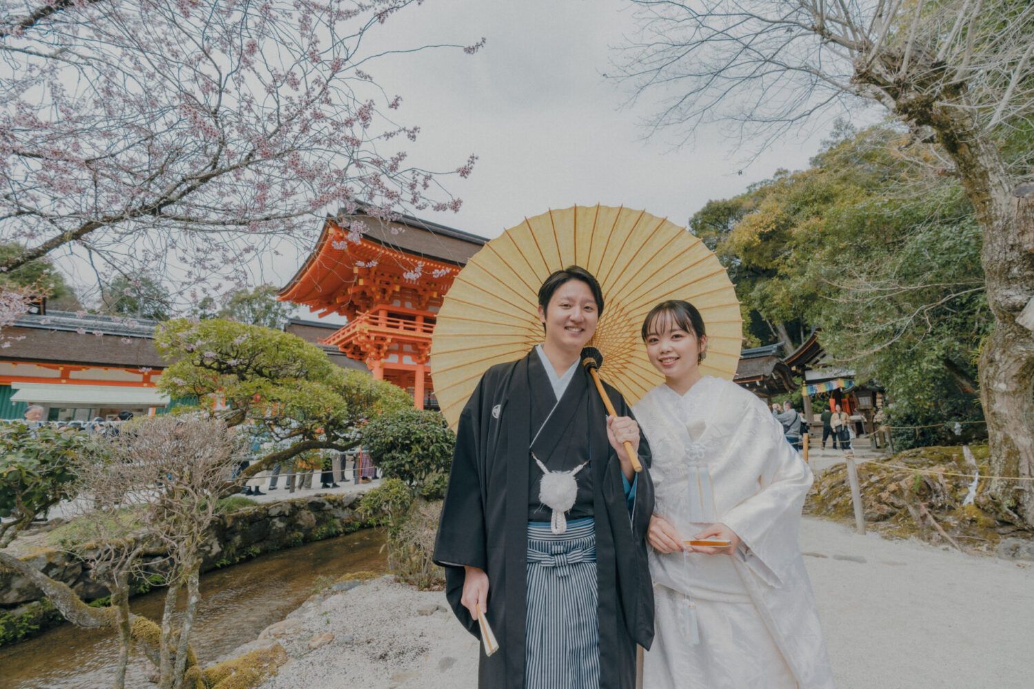 上賀茂神社の桜門を背景に白の番傘を持ったで白無垢の花嫁と新郎