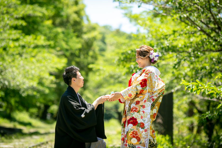 蹴上インクラインを背景に、紋付袴の新郎が片膝をついてプロポーズをしている。華やかな黄色地の色打掛を着た新婦が、新郎の手を取って微笑んでいる。