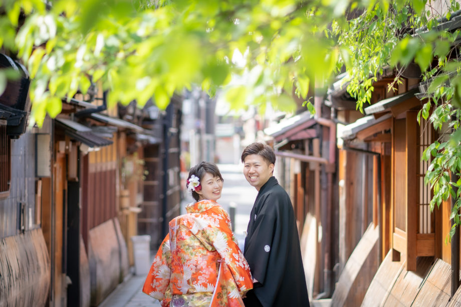京都の町を寄り添って歩く、色打掛をまとったショートヘアの花嫁と紋付き袴の新郎