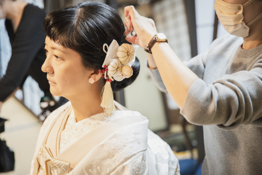 ウエディングフォト:白無垢に合わせ、繊細で可愛らしい和装髪飾りを丁寧に取り付けてもらう新婦の横顔です。