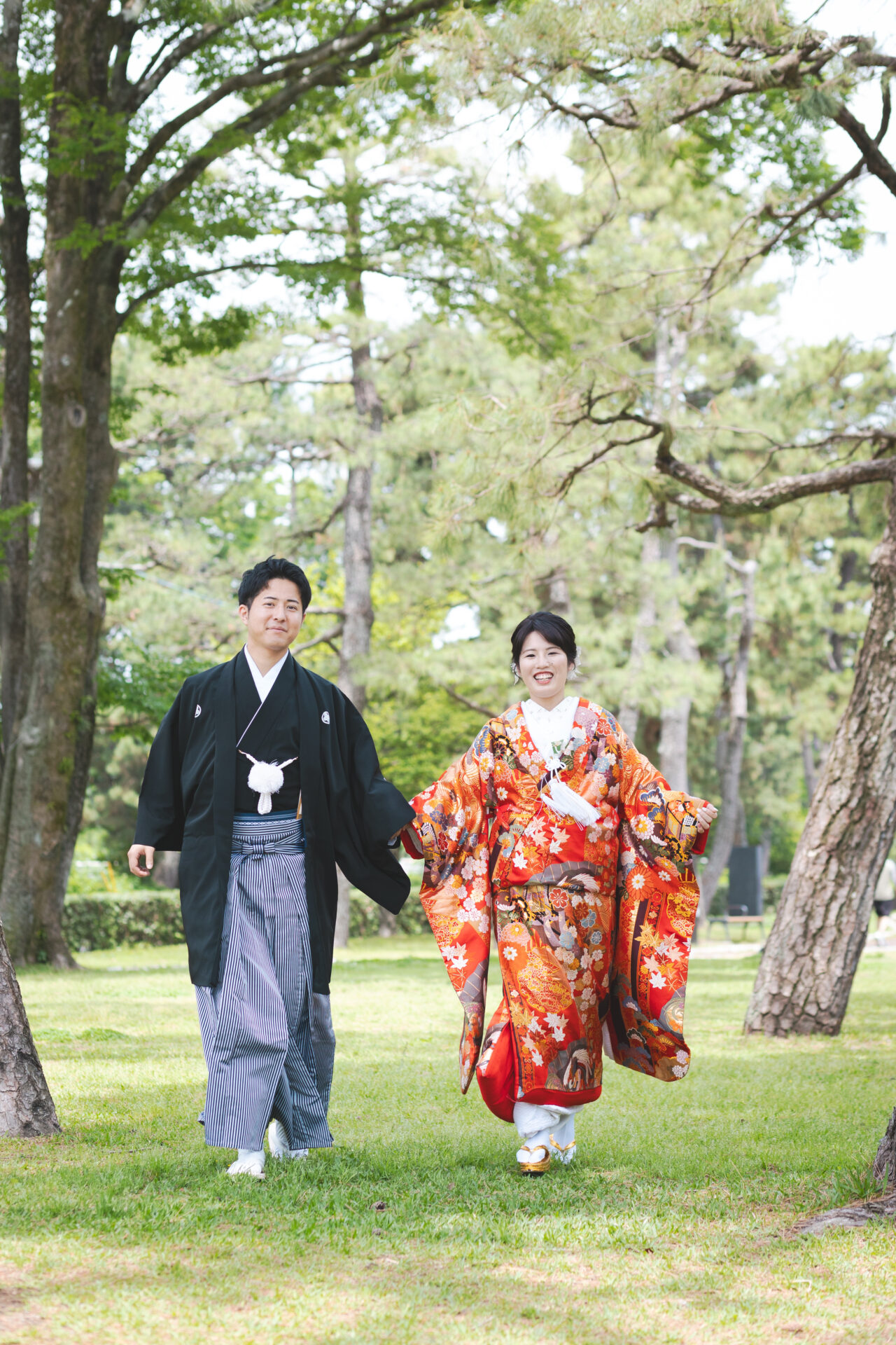 京都フォトウェディング
鴨川デルタ
緑がまぶしい糺の森を抜けて、賀茂川と高野川が合流するこの場所は、京都らしい情緒とナチュラルな美しさが溶け合う人気の撮影スポットです。

色打掛は、赤を基調に四季の花々が描かれた華やかな一着。新緑とのコントラストがとても美しく、思わず見とれてしまうほど。
石の飛び石を渡るおふたりの姿には、どこか懐かしさと新しさが同居していて、まるで映画のワンシーンのようでした。

川辺で並んで腰掛け、そっと手をつなぐカット。
ふと笑い合う自然な表情も、風にそよぐ髪や打掛の揺れもすべてが絵になります。

鴨川デルタの撮影は、自然体で、でもどこか特別。
おふたりの時間がゆっくりと流れていくような、そんな優しいフォトウェディングとなりました。