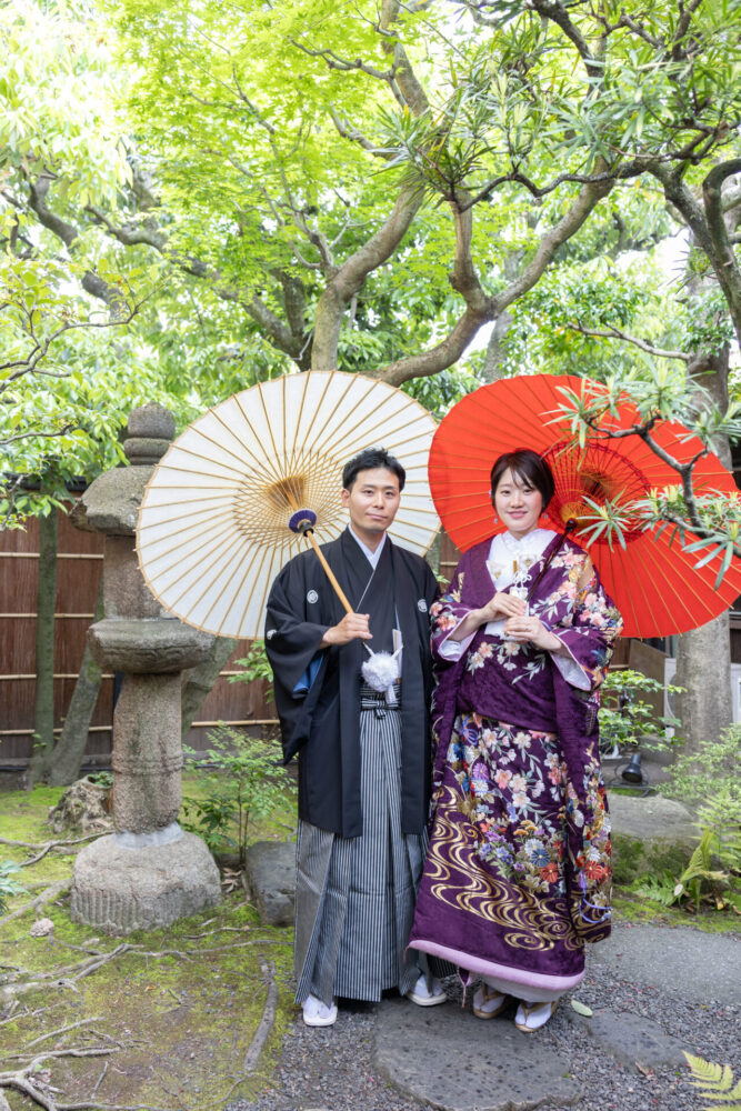 【紫の色打掛と番傘で楽しむ、京町家お庭フォト】

京都町家寫眞館のお庭にて、新郎新婦が並んで番傘を手にした印象的なワンシーン。
新婦様は深みのある紫の色打掛をまとい、優雅な雰囲気に。
新郎様の和装と紅白の番傘を差せば、ふたりだけの物語が始まるような、情緒あふれるひとときに。

京町家ならではの緑に囲まれた庭と、伝統小物が織りなす風情が、和装フォトウェディングにぴったり。
京都らしい趣を大切にしたいおふたりにおすすめのフォトウェディングです。