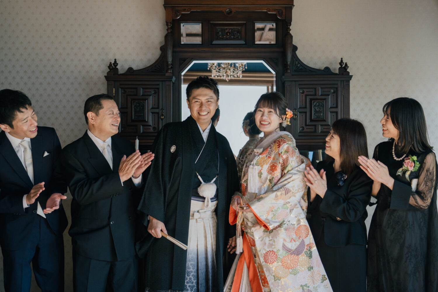 京都町屋寫眞館の京町屋スタジオにて、色打掛の新婦と新郎を家族が拍手で祝福する、幸せあふれる家族フォトウェディングの瞬間。