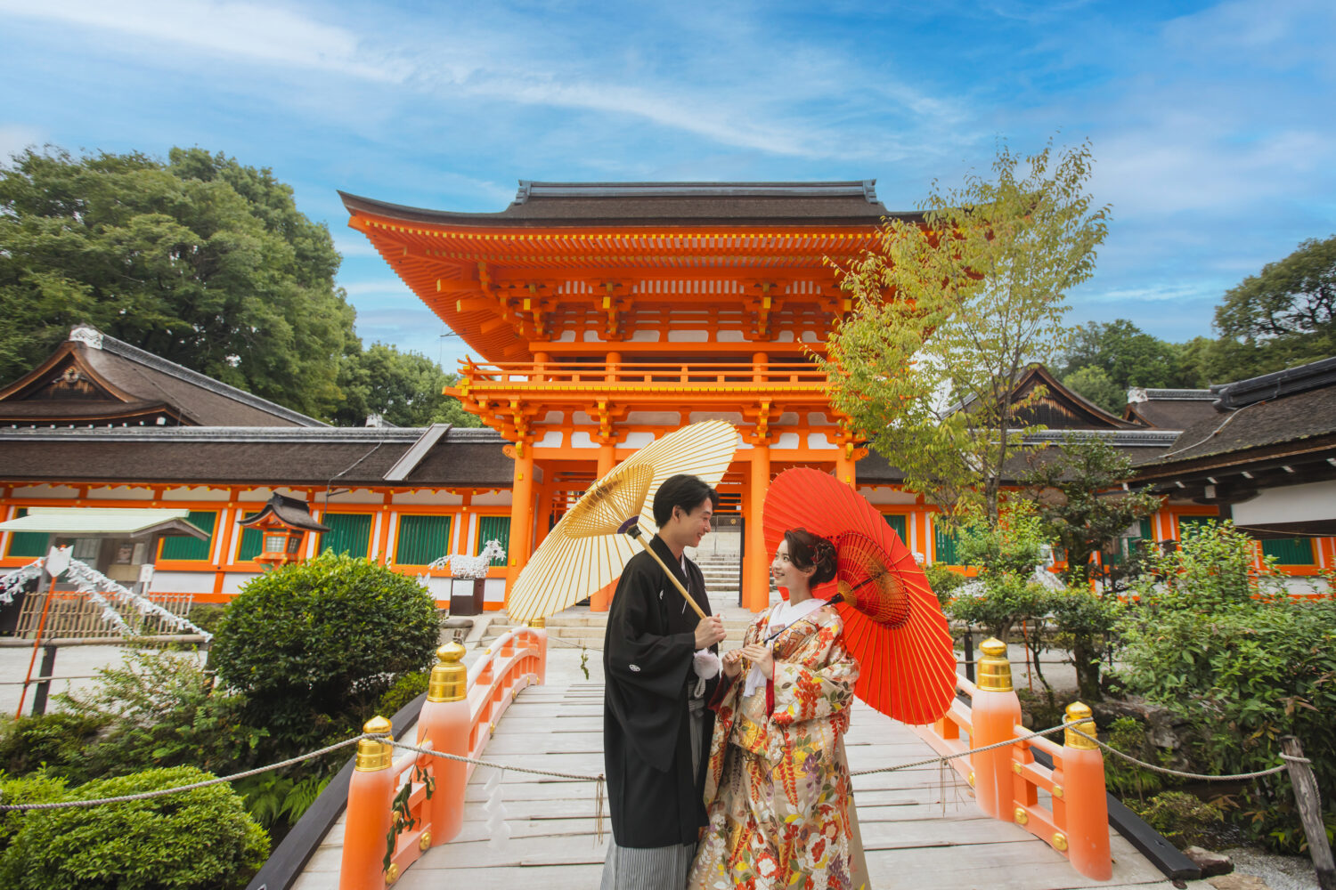 神社の楼門前で和傘を持つ新郎新婦のロケーションウェディングフォト