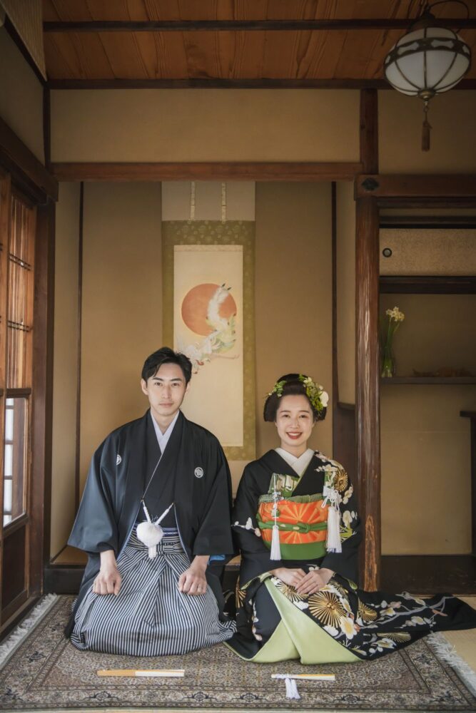 京町家の和室にて。正座で微笑む黒引き振袖の花嫁と新郎。