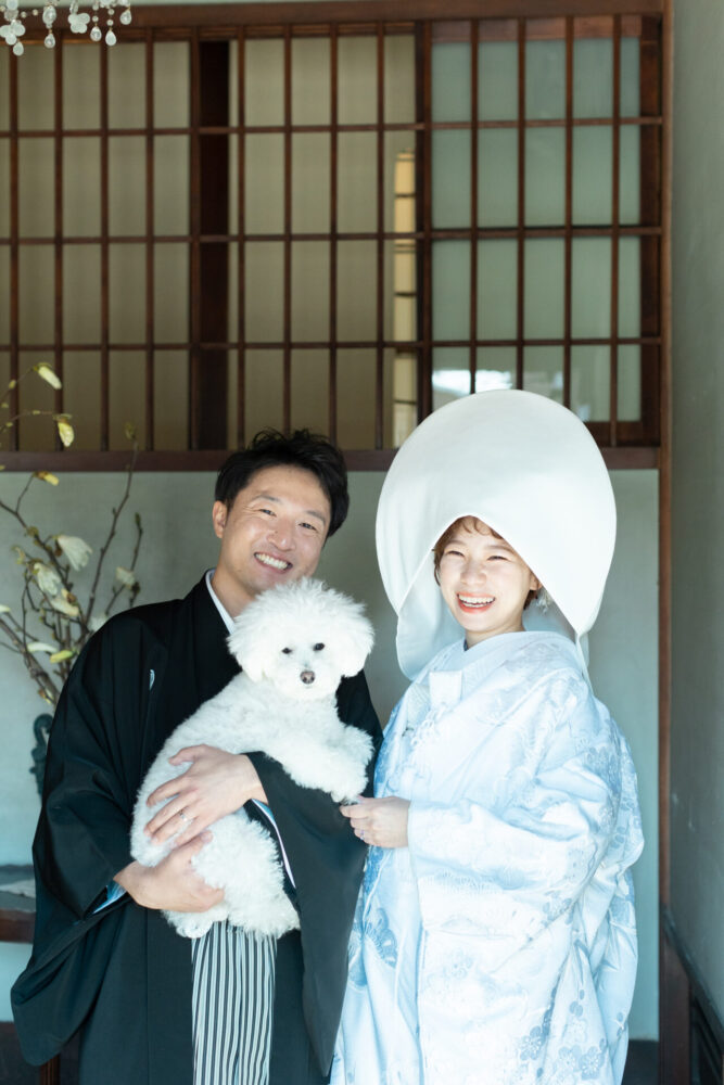 白無垢姿の花嫁と黒紋付の新郎が愛犬を抱いて笑顔を見せるウェディングフォト