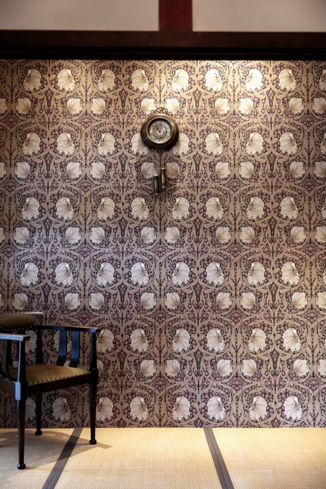 ウィリアム・モリスの「ピンパーネル」柄の壁紙に、畳・アンティークの木製椅子と壁掛け時計が並ぶスタジオセット。 明治・大正期の洋館のような情緒漂う空間。