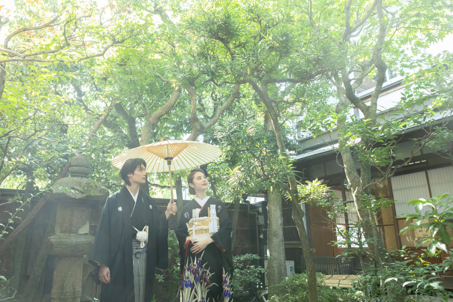 京町家の日本庭園で和傘をさす新郎と黒引き振袖の新婦。古民家ならではのレトロな和装フォトウェディング。