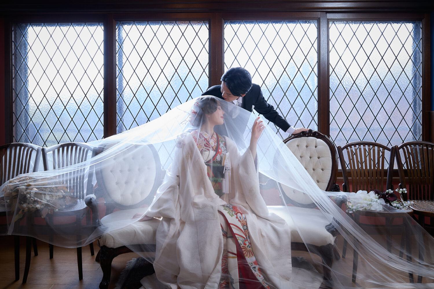 ステンドグラスのある洋館風スタジオで、ベールに包まれた和装の花嫁と新郎