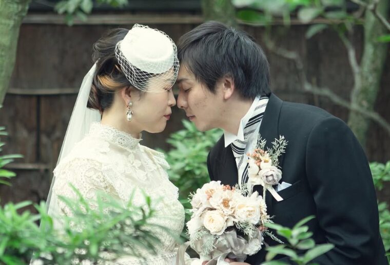 レースのヴィンテージドレスとトーク帽を合わせた花嫁と新郎の、額を合わせたレトロなアップ写真