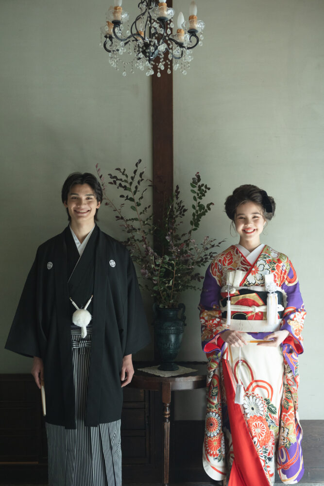 アンティークな京町家で微笑む新郎新婦。 新婦は鮮やかな紫に大輪の菊が描かれた婚礼衣装に黒リボンを合わせ、新郎は紋付袴で凛とした佇まい。