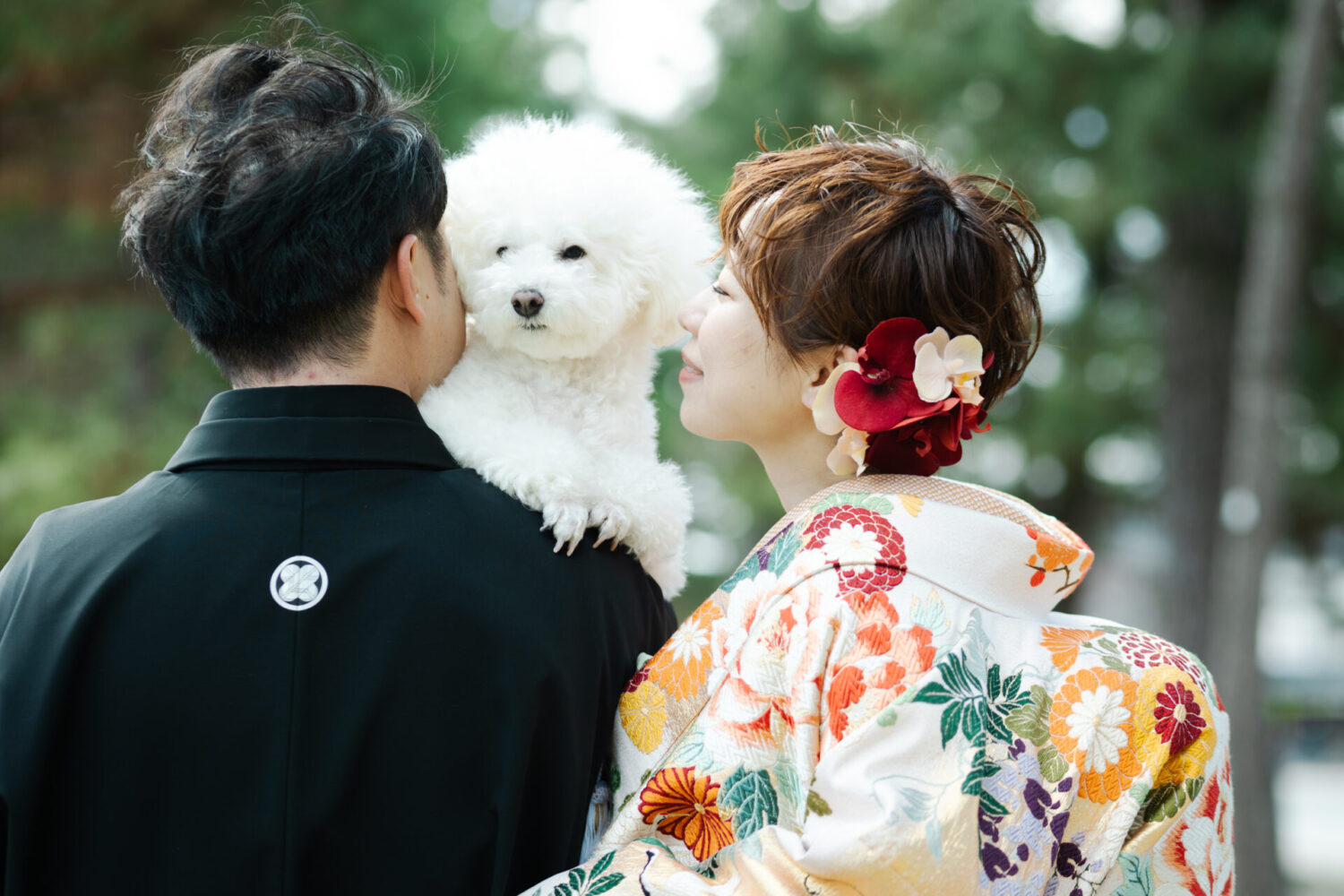 色打掛姿の新婦と黒紋付の新郎が、白いトイプードルを抱きながら屋外で寄り添う後ろ姿
