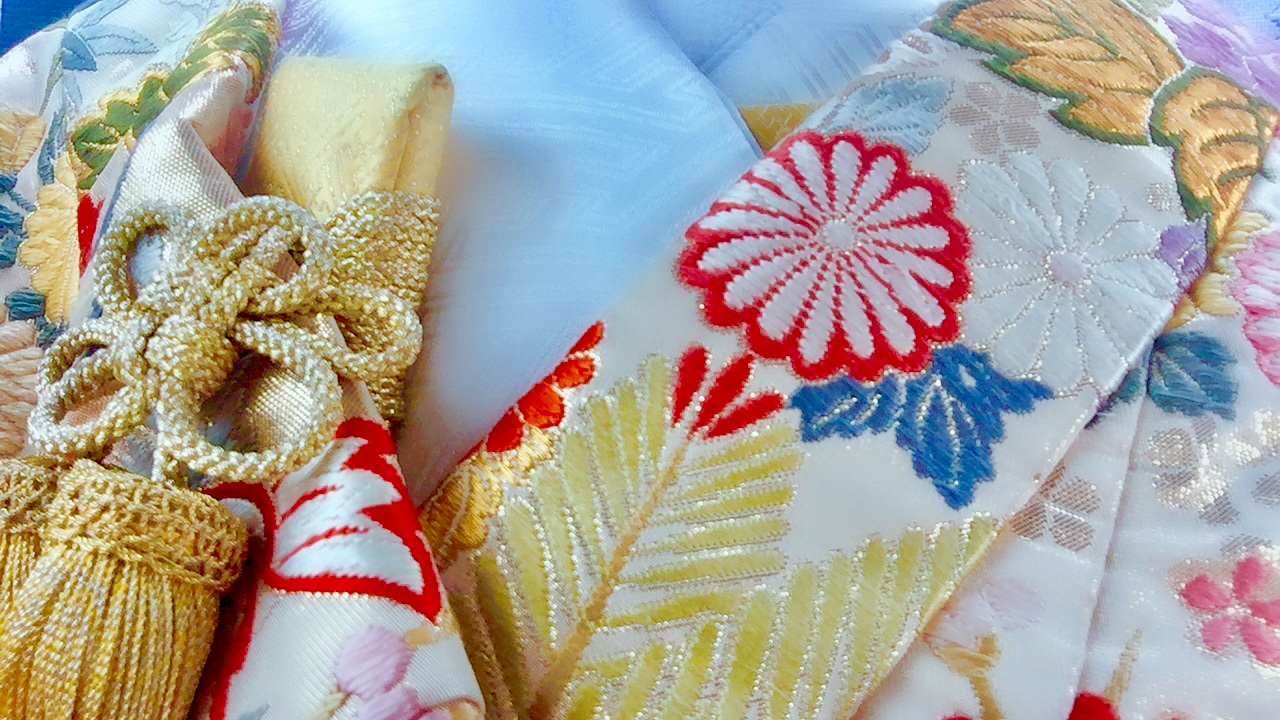 華やかな刺繍が施された着物の帯と、金色の組紐が美しい和装小物のクローズアップ。