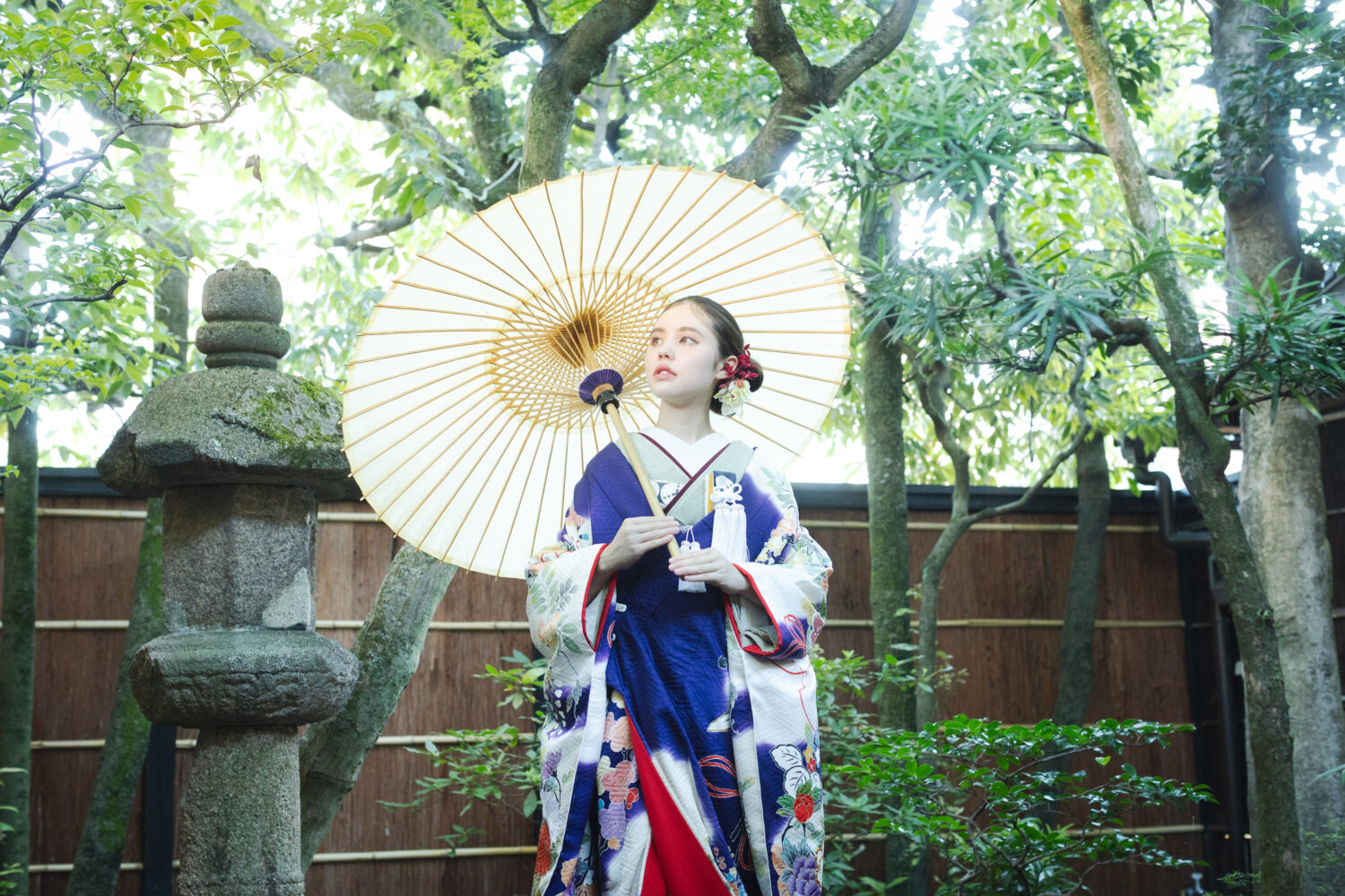 京都町家寫眞館の日本庭園で、和傘を差し凛とした表情を浮かべる和装の花嫁。 アンティーク柄の引き振袖と、胸元の懐剣・筥迫などの小物がレトロな世界観を演出します。