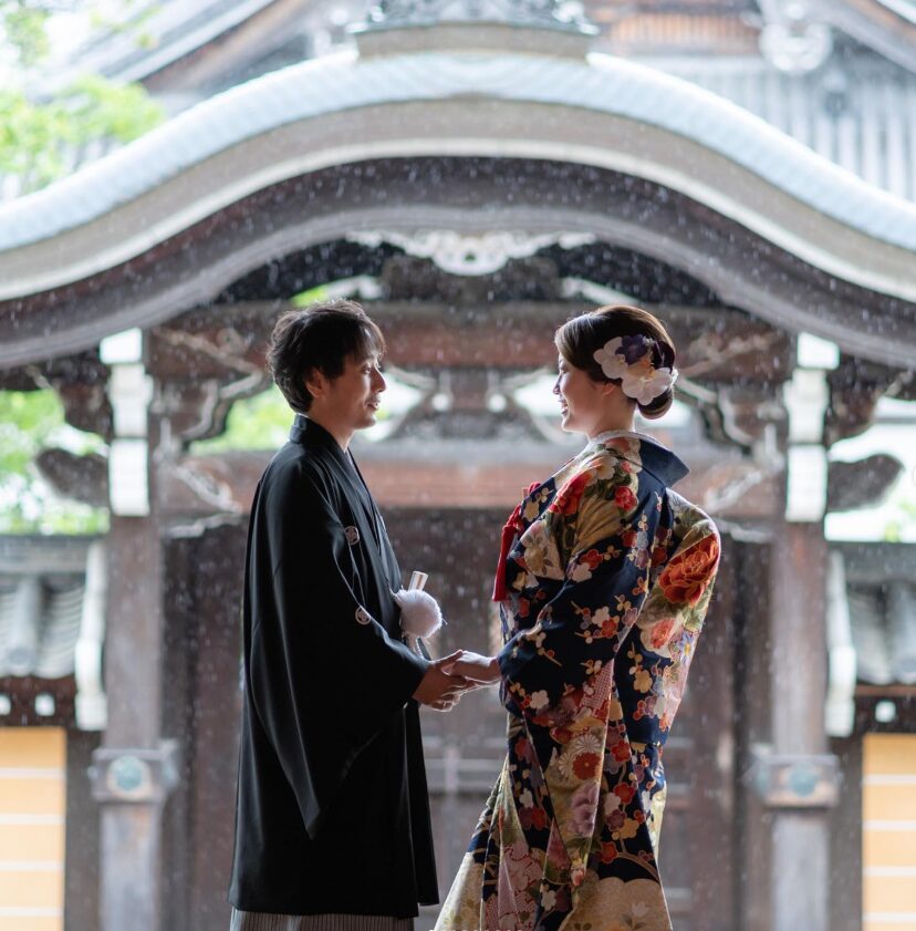 京都の風情ある金戒光明寺を背景に見つめ合う、黒紋付姿の新郎と色打掛姿の新婦の和装前撮りショット。雨が降っている