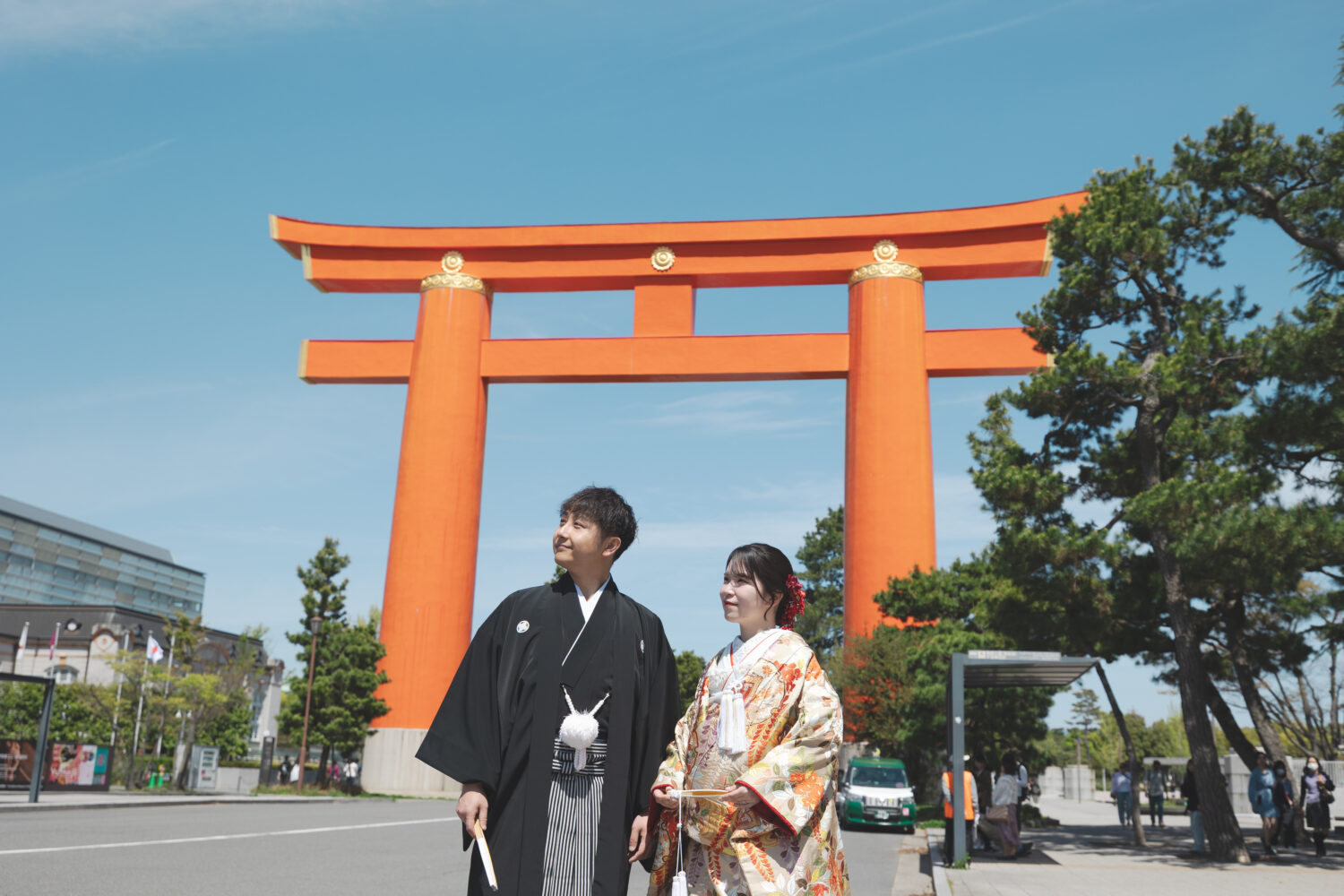 平安神宮の大鳥居を背景に、青空の下で並ぶ色打掛と紋付羽織袴の新郎新婦の和装前撮り