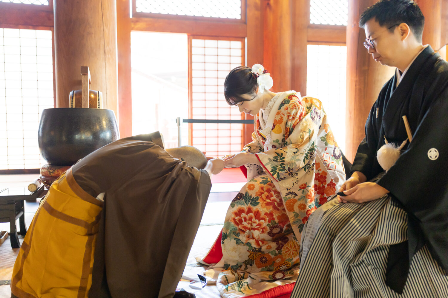 金戒光明寺の本堂で僧侶から授かりものを受ける、色打掛と紋付羽織袴の新郎新婦の仏前式